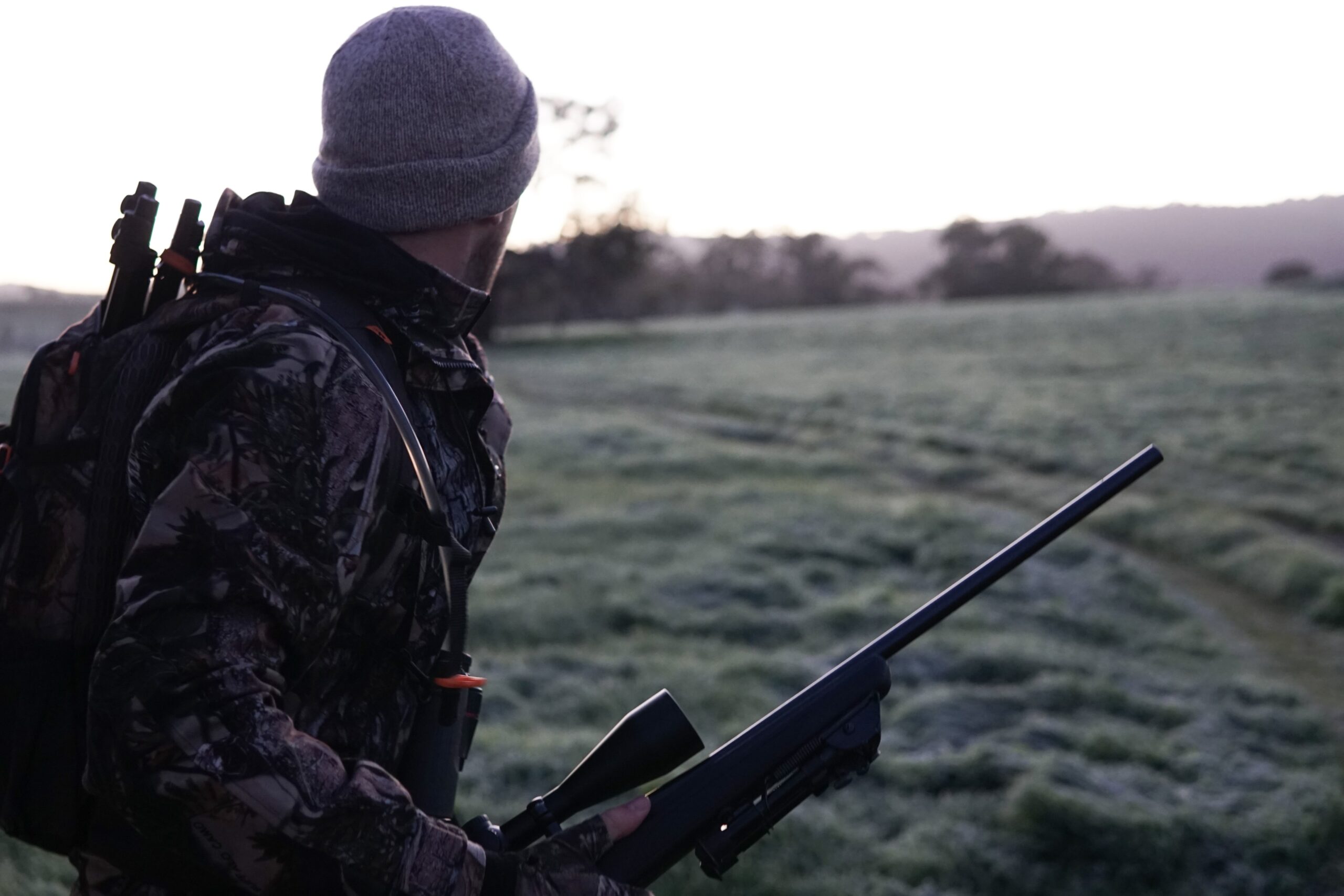 Hunter with hunting gear in an open field holding a hunting rifle.