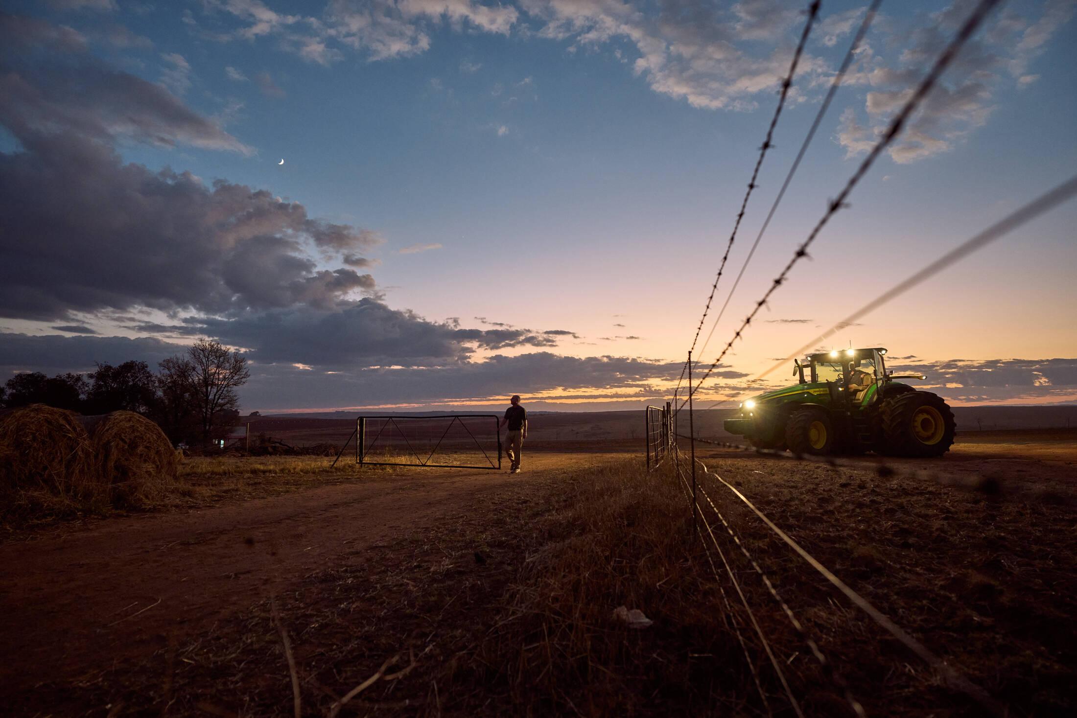 South African farmer at a farm gate at dusk with tractor lights in the background, highlighting the critical importance of rural security and firearm law changes.
