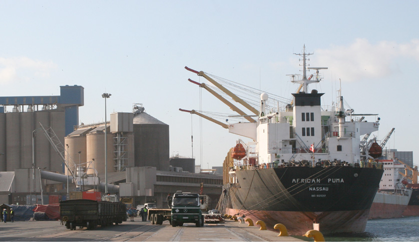 Cargo ship docked alongside grain-handling facilities at Durban harbour, South Africa, illustrating the global crossfire of rising shipping costs, international grain trade disruptions and wheat import pressures affecting South African agriculture and food prices in 2027.